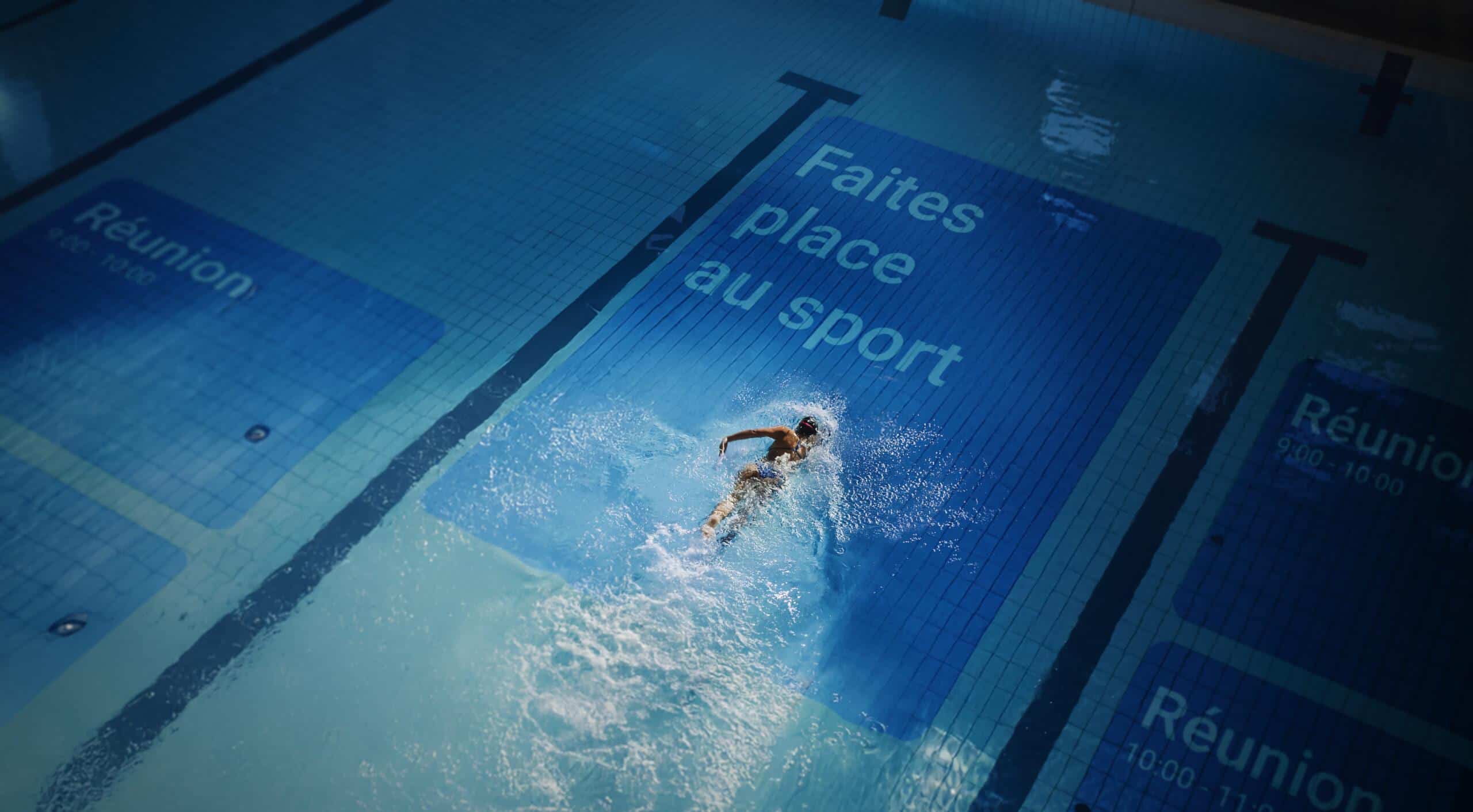 Person swimming in a pool with "Faites place au sport" banner.